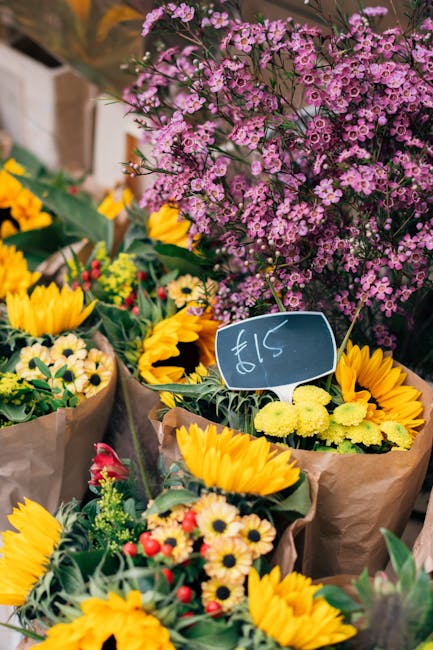 A vibrant display of fresh floral bouquets arranged with a variety of flowers, including cheerful yellow sunflowers with large, round petals, small white daisies, and red and yellow buds, all wrapped 